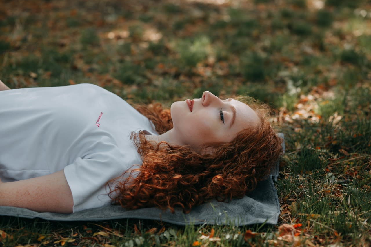 teen girl with red hair lying in grass with closed eyes